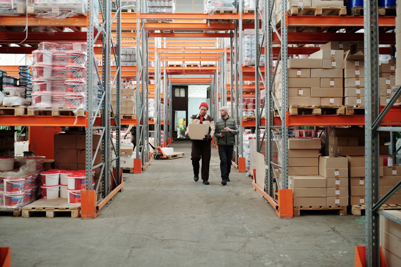 Crafting Captivating Headlines: Your awesome post title goes here Two workers handle a package in a spacious warehouse surrounded by shelves stocked with boxes and products.